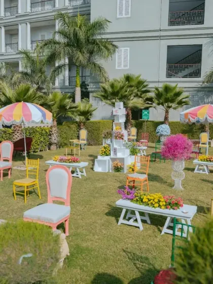 A whimsical photo-op area at the colorful Haldi, with mismatched vintage chairs scattered on the lawn, inviting guests to interact with the decor.