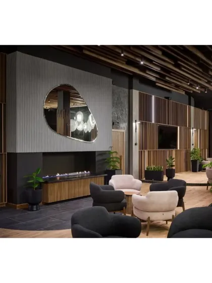 A seating area in the lounge with a modern fireplace and a large, organically shaped mirror, set against a backdrop of slatted wood panels.