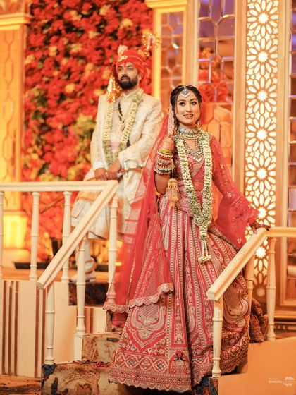 Posed against a backdrop of red roses, the couple looks like royalty. This shot highlights their magnificent wedding outfits and the grandeur of the decor.