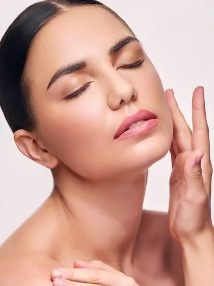 A classic beauty headshot with a focus on natural, glowing skin. The model's pose, with her hand gently touching her face, feels soft and serene, perfect for skincare or wellness brands.