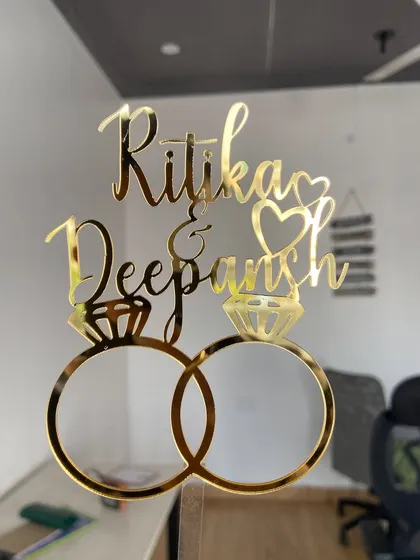 Holding up the "Ritika & Deepansh" topper to show its size and the brilliant shine of the gold acrylic.