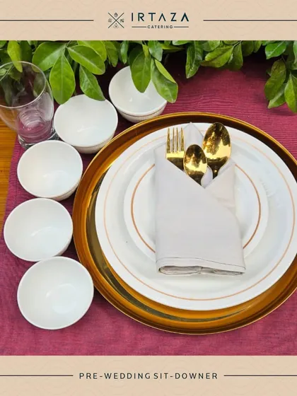 A detailed place setting from a pre-wedding sit-down dinner. The golden cutlery, gold-rimmed plate, and clean white bowls showcase a commitment to elegance in every detail.
