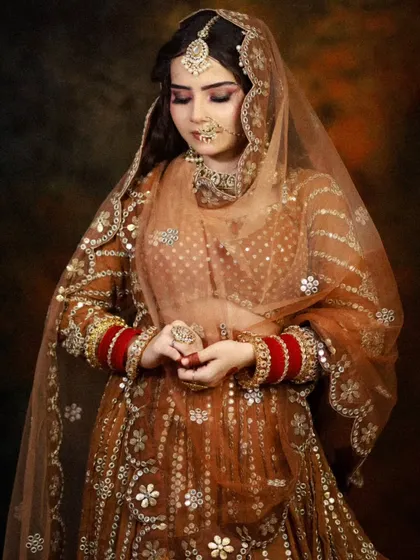 A demure pose that highlights the intricate embroidery on the lehenga and the delicate henna on her hands. The makeup is kept subtle to complement the rich details.