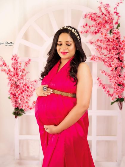 A close-up portrait focusing on the beautiful mother-to-be. The bright pink gown and floral background create a joyful and feminine atmosphere.