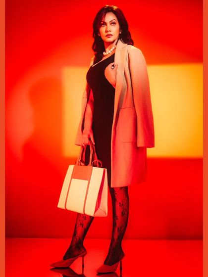 A high-fashion commercial look. The dramatic red background with a focused spotlight creates a powerful, energetic feel that makes the entire outfit, from the coat to the handbag, stand out.