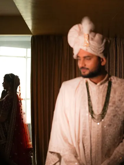 An artistic shot with the bride in silhouette by the window and the groom in the foreground, creating a layered and story driven portrait.