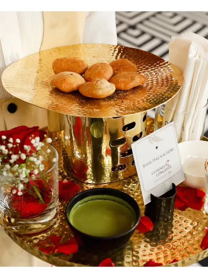 A server holds a tray with Bedmi Puri and Aloo, presented in an elegant golden serving set. We elevate even the most traditional dishes with luxurious serveware and thoughtful presentation.