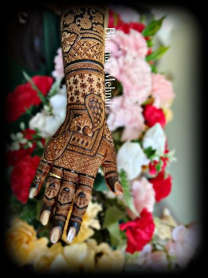 A close up of a bridal hand against a backdrop of flowers, highlighting the intricate details. This design features an elephant motif, delicate check patterns, and fine line work for a classic and elegant bridal style.