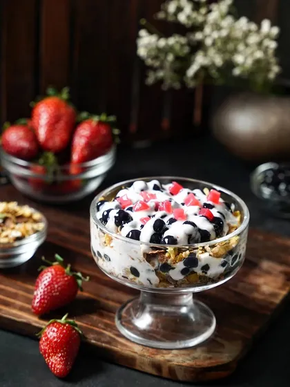 A healthy and delicious boba parfait with layers of cereal, yogurt, and fresh strawberries. The rustic wooden board and dark background create a wholesome yet indulgent feel.