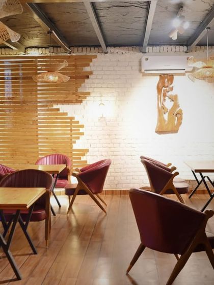 The interior design features a mix of textures, from the exposed brick wall to the wooden slats and modern chairs, creating a visually interesting and comfortable dining space.