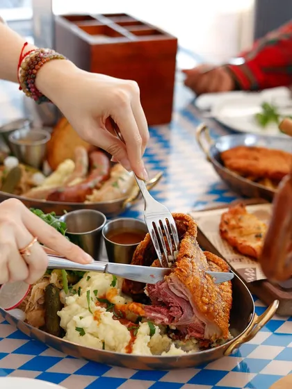 Capturing the moment of enjoyment. A knife and fork cutting into a crispy pork knuckle shows the texture and makes the dish feel interactive.