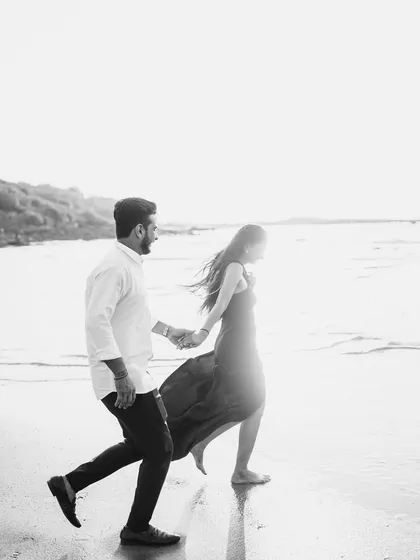 A high-contrast black and white photo of a couple running along the shoreline. The bright light and sense of motion give this image a free-spirited and timeless feel.