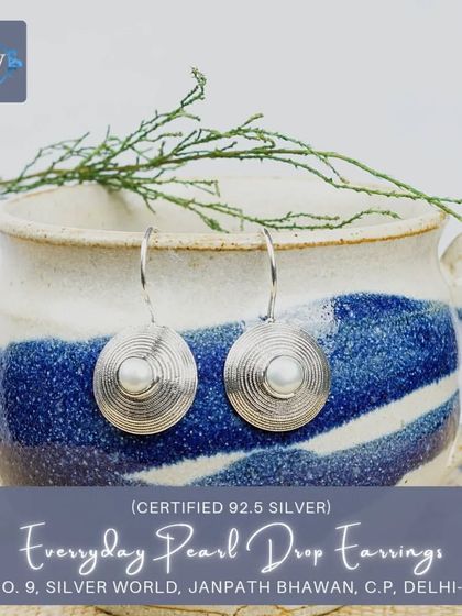 These modern-ethnic drop earrings have a pearl at the center of a textured, spiral-patterned silver disc, offering a contemporary take on classic pearl jewelry.