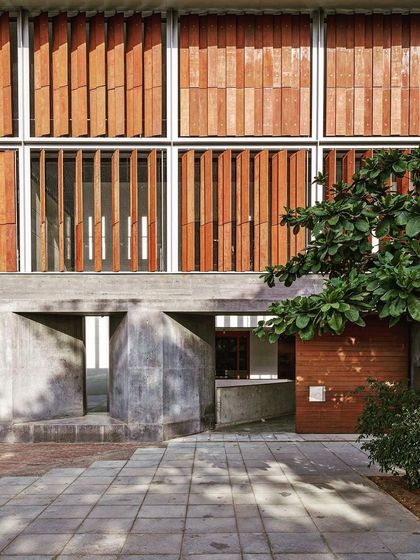 A detail of a facade with operable wooden louvers set within a concrete frame. This system allows occupants to control the amount of light and air entering the space, making the building adaptable to changing conditions.