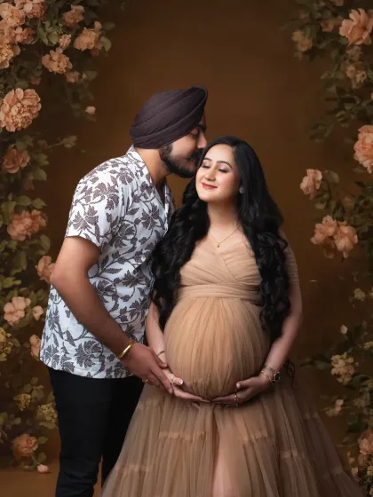 A tender moment in a floral wonderland. The father-to-be gently kisses his partner's cheek, surrounded by a beautiful arch of rustic-toned flowers.