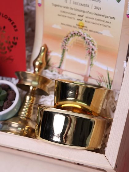 A close-up on the traditional brass items included in the wedding invitation hamper, symbolizing light and prosperity for the new beginning.