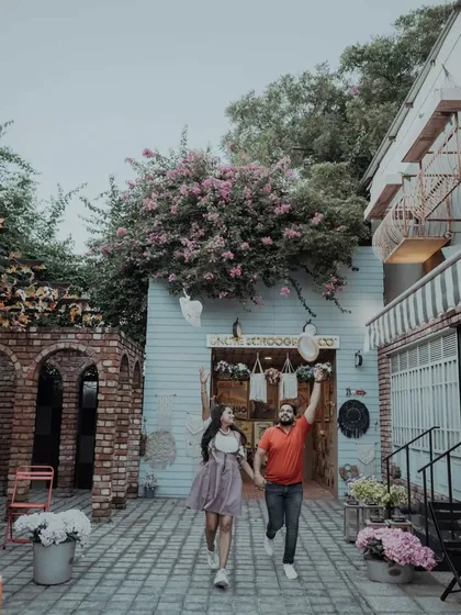 A joyful, energetic shot of the couple running through a charming, European-style alley. The flowers and architecture create a whimsical and happy atmosphere.