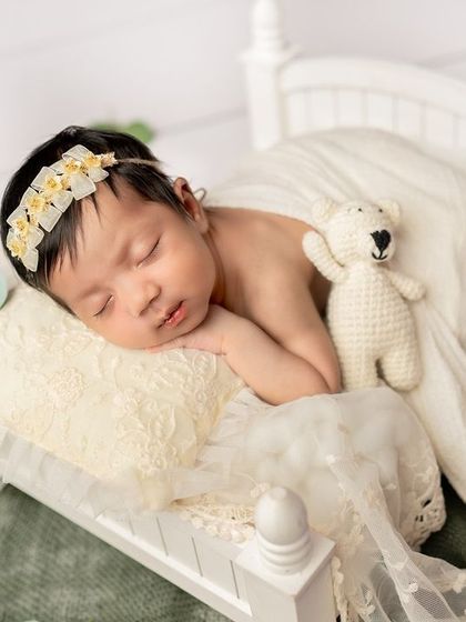 Dreaming peacefully with a little teddy bear friend. The combination of the white lace, soft fabrics, and floral headband creates a truly ethereal portrait.