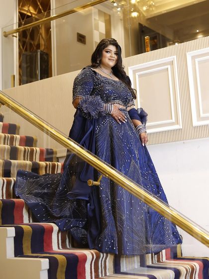 A plus-size client looking absolutely regal in a navy blue lehenga, posing on a grand staircase. The outfit is customized to fit her perfectly.