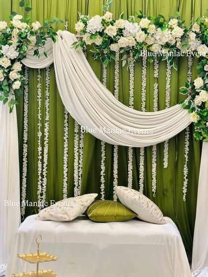 An elegant Mehendi setup with an olive green and white color scheme. The backdrop features beautiful white floral arrangements and hanging strings of mogra against the rich green fabric.