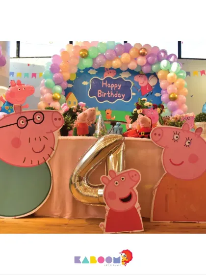 A fun-filled Peppa Pig party setup for a fourth birthday, complete with large cutouts of Peppa and Daddy Pig, a pastel balloon arch, and a themed dessert table.