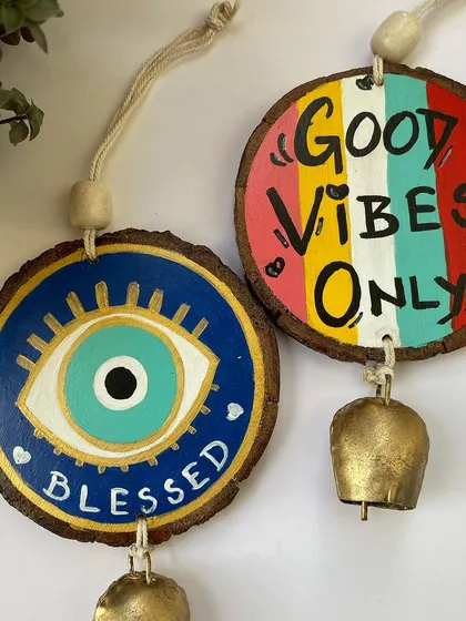 Bring in some good vibes with my hand-painted wooden hangings. This set features the popular evil eye design to keep your home blessed and a colorful "Good Vibes Only" quote, complete with rustic iron bells for a charming sound.