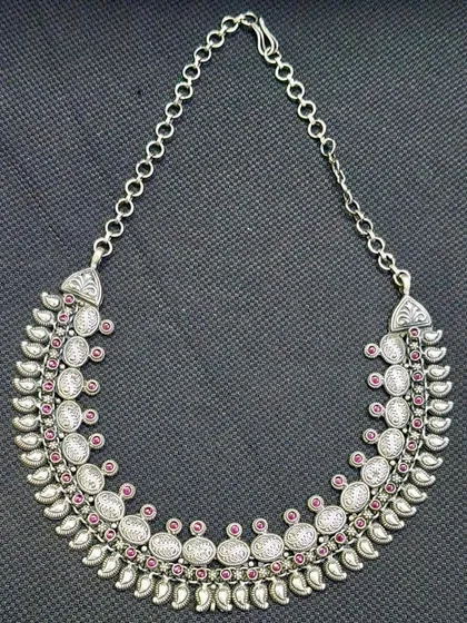 A premium pure silver necklace with a traditional flair. This crescent-shaped piece features repeating motifs studded with pink stones, creating an elegant collar-style necklace.