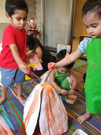 Children working together to paint a large paper mache Ganesha idol. This collaborative project teaches them about teamwork and the joy of creating together.