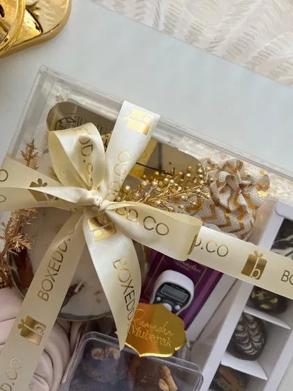A luxurious acrylic box filled with Ramadan essentials like a Tasbeeh counter, dates, and chocolates, all tied with a custom branded ribbon.