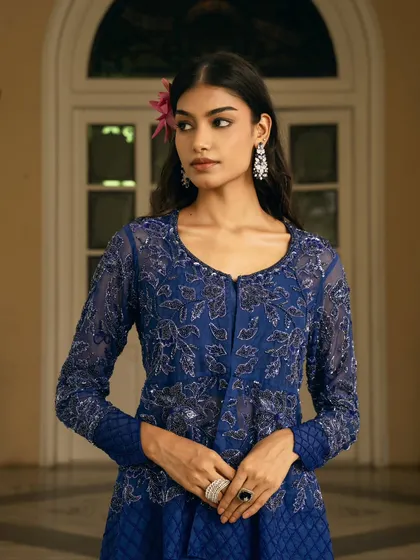 A medium close-up focusing on the rich texture and floral embroidery of a royal blue jacket-style top. The soft lighting and the model's direct gaze create a powerful and intimate portrait.