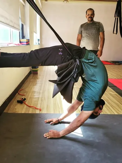 A student holds a deep backbend against the wall with a prop for support. This method allows for a longer hold, increasing the therapeutic benefits for the spine.