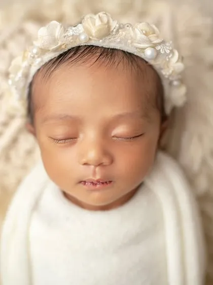 Pure and simple. A sleeping newborn in a white wrap, adorned with a floral headband, showcases their natural beauty.