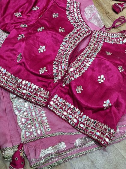 A closer look at a custom-stitched pink blouse with a keyhole back design. The intricate mirror work on the neckline and sleeves is designed to perfectly complement the client's saree for a wedding function.