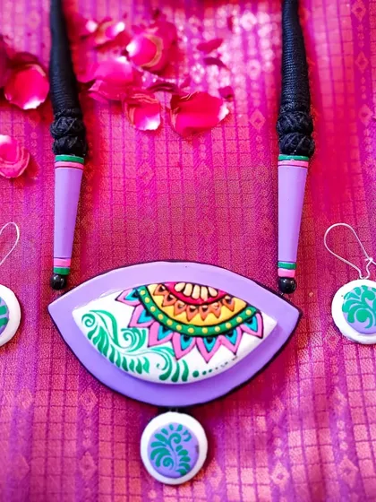 A duplicate image of the lavender and green eye-shaped pendant, set against a rich purple silk background.