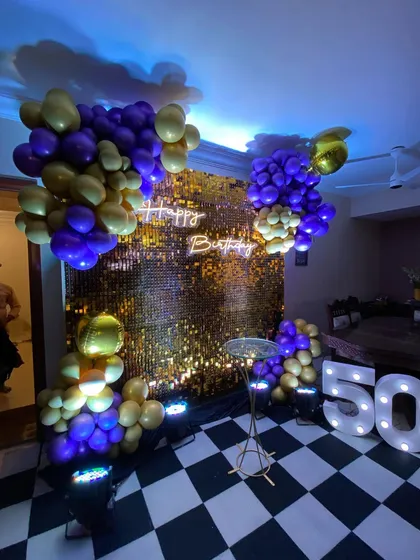 Celebrating a 50th birthday in style. This setup features a shimmering gold sequin wall, a custom "Happy Birthday" neon sign, and bold marquee numbers, all brought together with a glamorous purple and gold balloon arrangement.