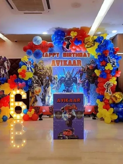 A vibrant Transformers theme for a 6th birthday. This decoration includes a large backdrop with characters, a marquee number '6', and a balloon arch in the classic red, blue, and yellow colors.