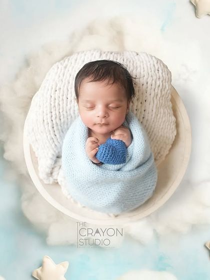 An overhead view of a baby wrapped in blue, sleeping on a bed of clouds and surrounded by stars, creating a dreamy, celestial scene.