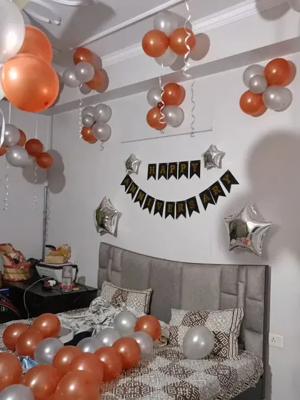 A simple and elegant bedroom decoration for a birthday. The room is decorated with orange and silver balloon bouquets on the ceiling and a 'Happy Birthday' banner over the bed.