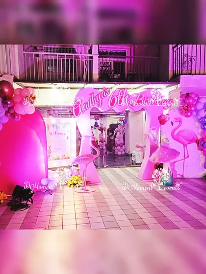 The entrance to the Flamingo-themed party, featuring a vibrant pink and purple balloon arch. Flamingo props and dramatic uplighting create an exciting and tropical welcome for guests.