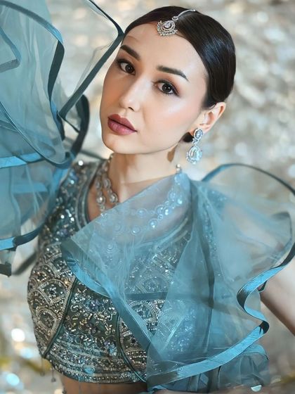A striking close-up of an international model wearing a blue lehenga with a dramatic ruffled dupatta. This is the kind of high-fashion look you can create by renting from me.