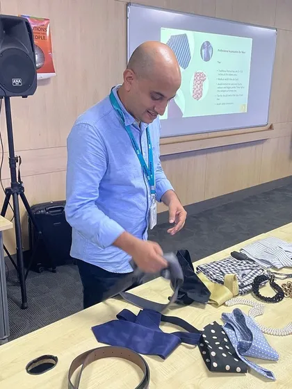 A participant engages in a hands on exercise about professional accessories, like ties. Understanding these details is key to mastering corporate dressing and projecting a polished image.