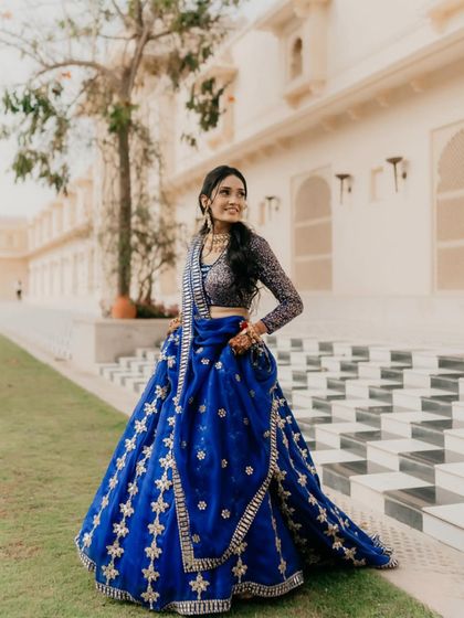 A full-length shot of the bride in her royal blue lehenga at The Oberoi Udaivilas. Her graceful pose and the stunning palace backdrop create a picture of regal elegance.