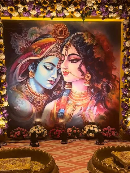 A closer view of the divine Radha Krishna backdrop. The rich colors of the painting are complemented by the vibrant floral frame, creating a perfect setting for a sacred Haldi function.
