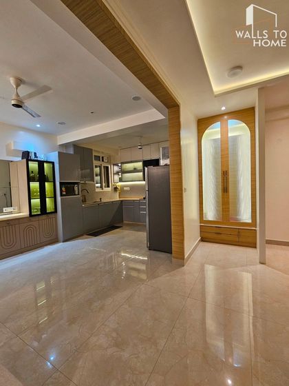 An open-plan living and kitchen area with a minimalist aesthetic. The grey kitchen cabinets and integrated bar unit create a cohesive and modern living space.