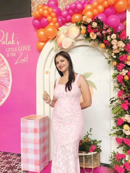 The happy mom-to-be at her vibrant citrus-themed baby shower. The decor features a bright pink and orange color scheme with a floral and fruit arch.