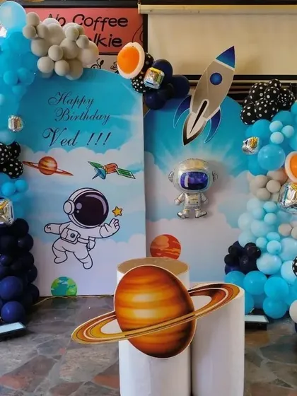 A space-themed birthday party with astronaut and rocket cutouts, planet props, and a balloon arch in shades of blue and orange.