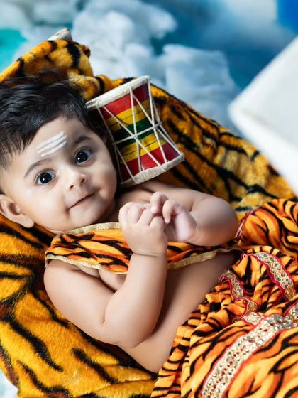 A sweet, curious look from this baby dressed as little Shiva, holding his damaru.