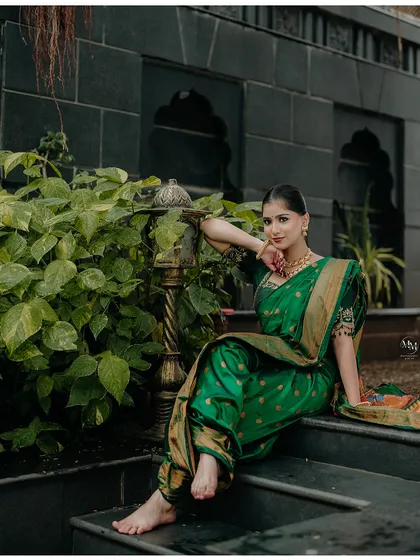 A stunning portrait of a bride in a traditional green Nauvari saree. Her pose against the dark, textured wall creates a beautiful contrast.