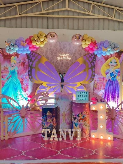 A magical princess and butterfly theme for a first birthday, with large butterfly wings as the centerpiece and cutouts of Cinderella and Rapunzel.