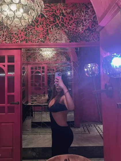 A mirror selfie in a vibrant pink bathroom, showcasing the daring back of the cutout dress.